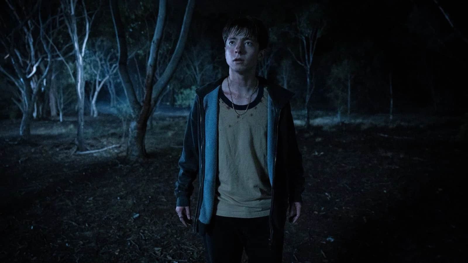 Adolescent au visage éclairé, debout dans une forêt sombre la nuit.