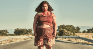 Femme aux cheveux bouclés debout sur une route, portant une tenue rose, avec des arbres en arrière-plan