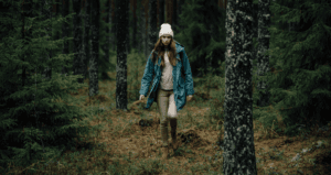 Femme marchant dans une forêt dense, vêtue d’une veste bleue et d’un bonnet blanc