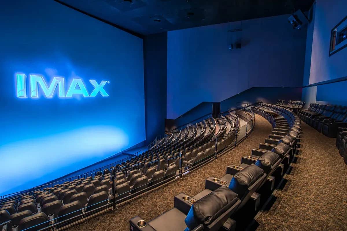 Salle de cinéma IMAX vide, avec écran géant bleu et rangées de fauteuils inclinables.