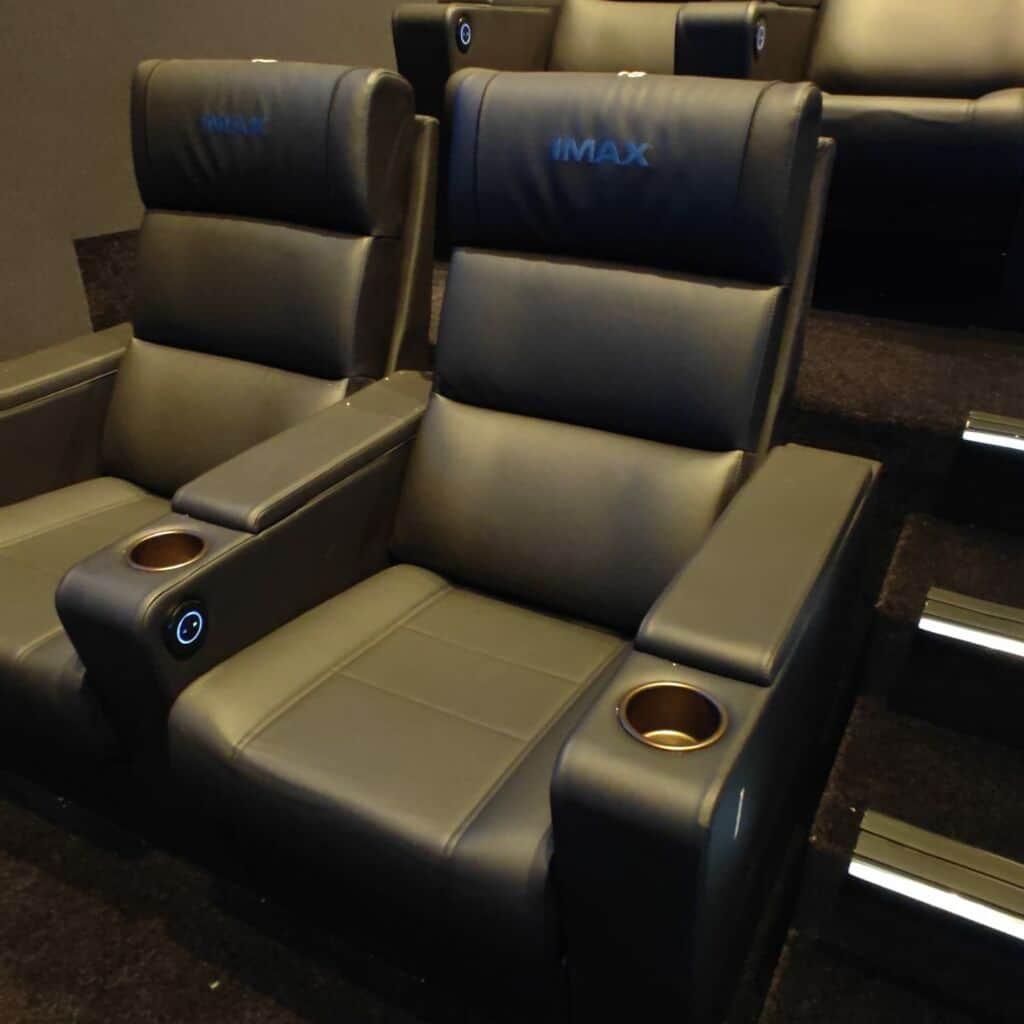 Deux fauteuils de cinéma en cuir avec porte-gobelets, marqués « IMAX » dans une salle sombre