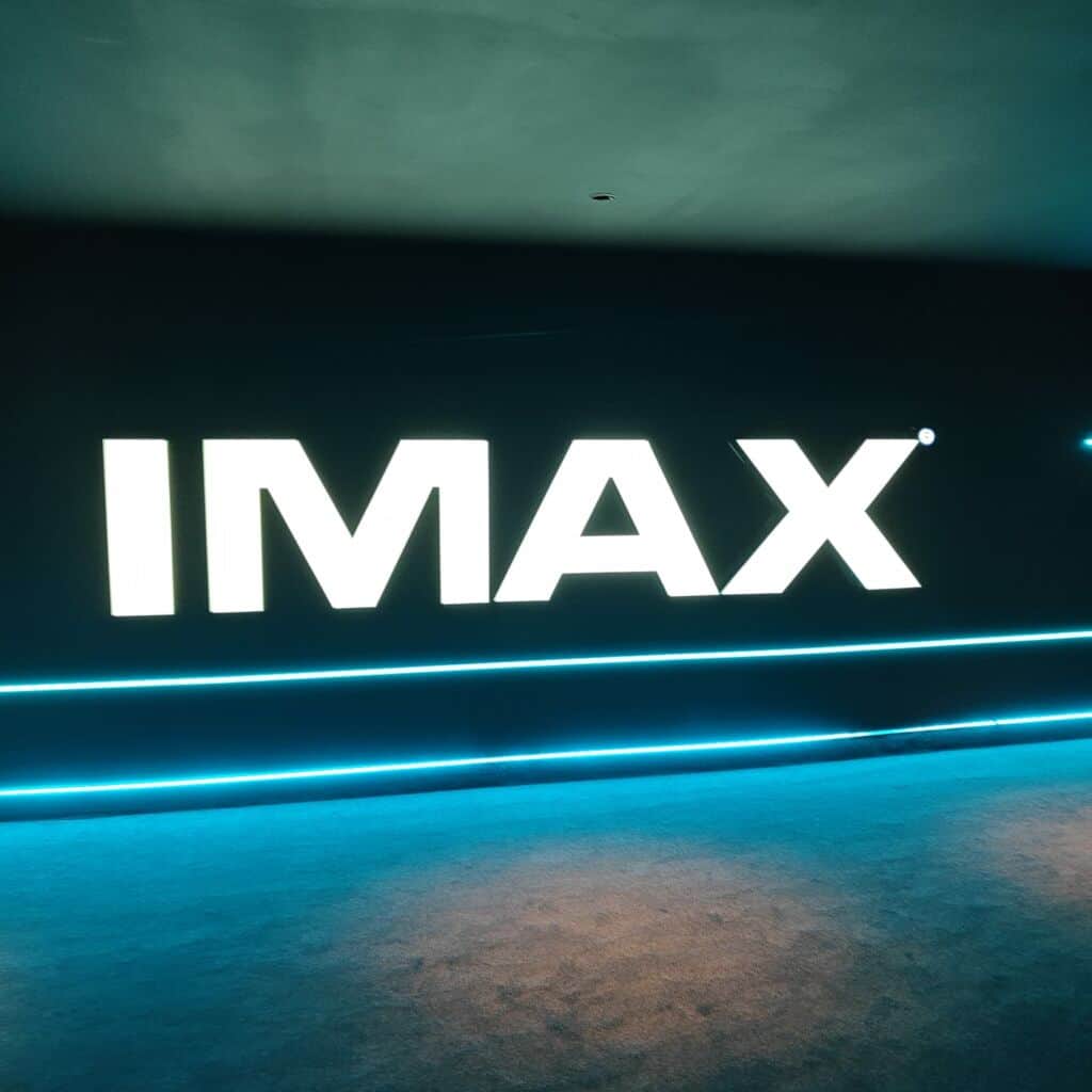 Affiche de « IMAX » avec un logo blanc lumineux sur fond sombre et des lignes bleues.