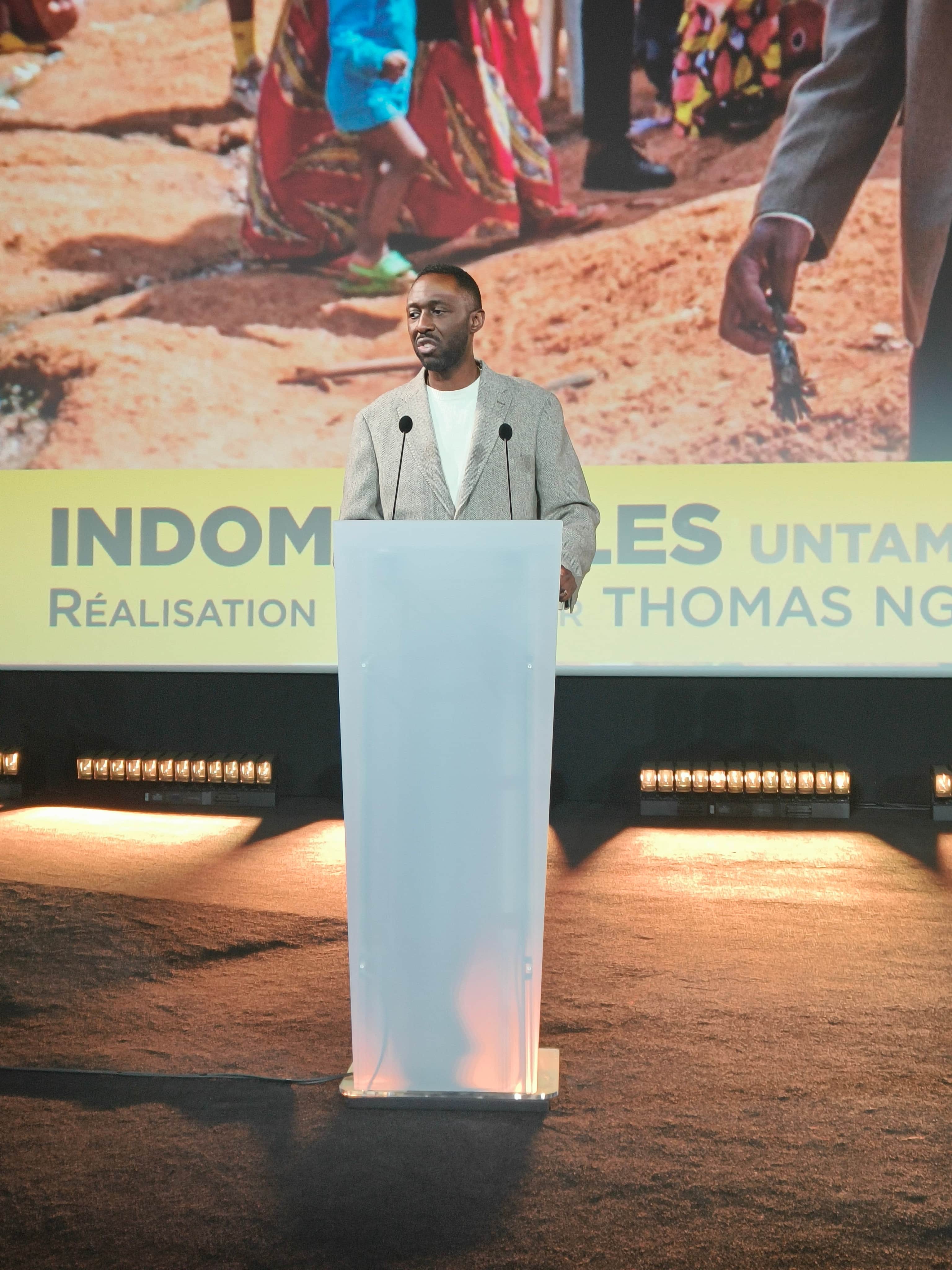 Affiche de « INDOMPTABLES » avec un homme devant un pupitre, sous une projection montrant des personnes en extérieur