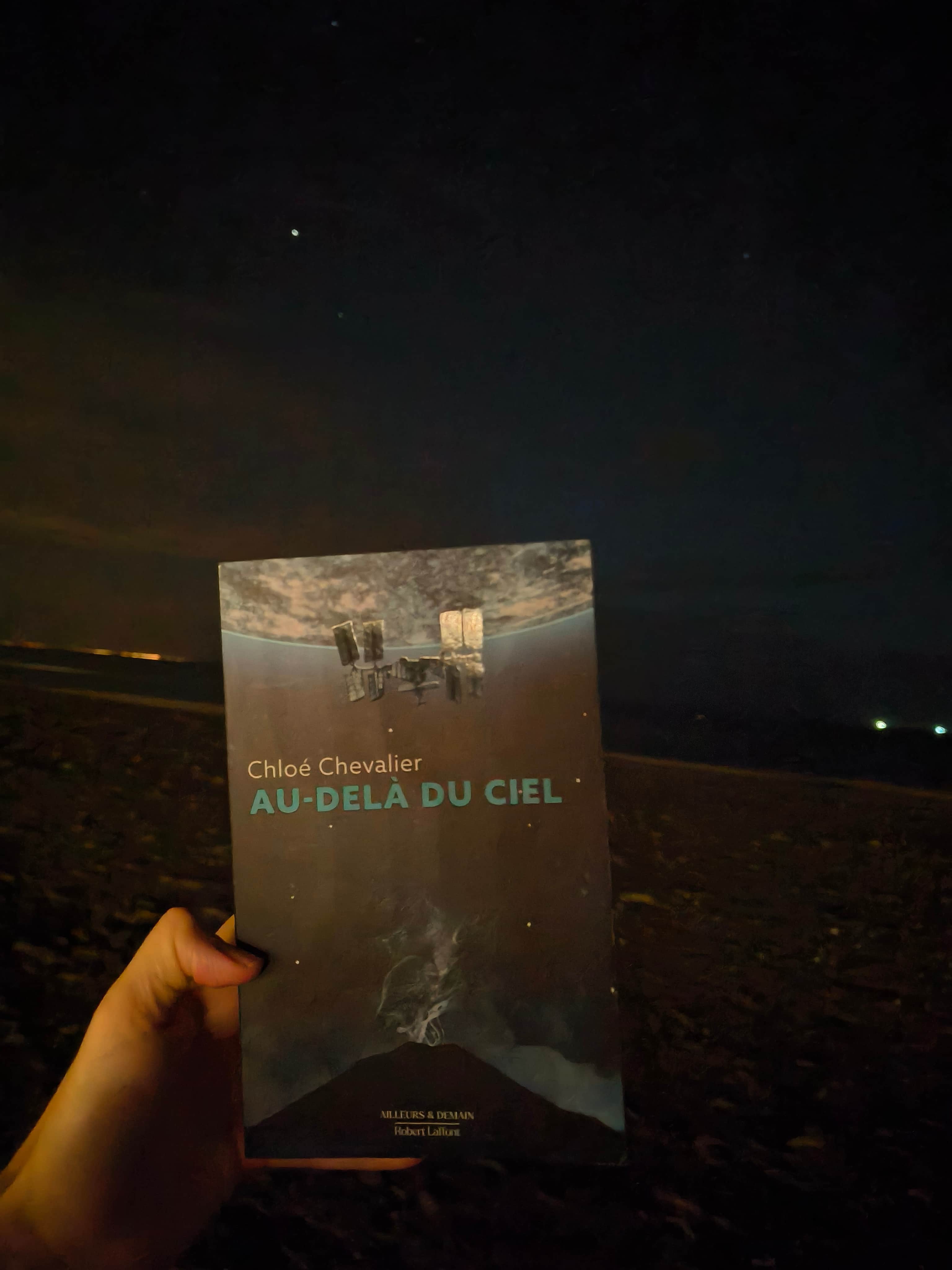 Jaquette de « AU-DELA DU CIEL » de Chloé Chevalier, avec une structure flottante au-dessus d’un paysage sombre.