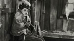 Un homme moustachu assis, coiffé d’un chapeau melon, dans un intérieur rustique