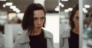 Femme aux cheveux bruns face à un miroir, dans un intérieur éclairé aux néons