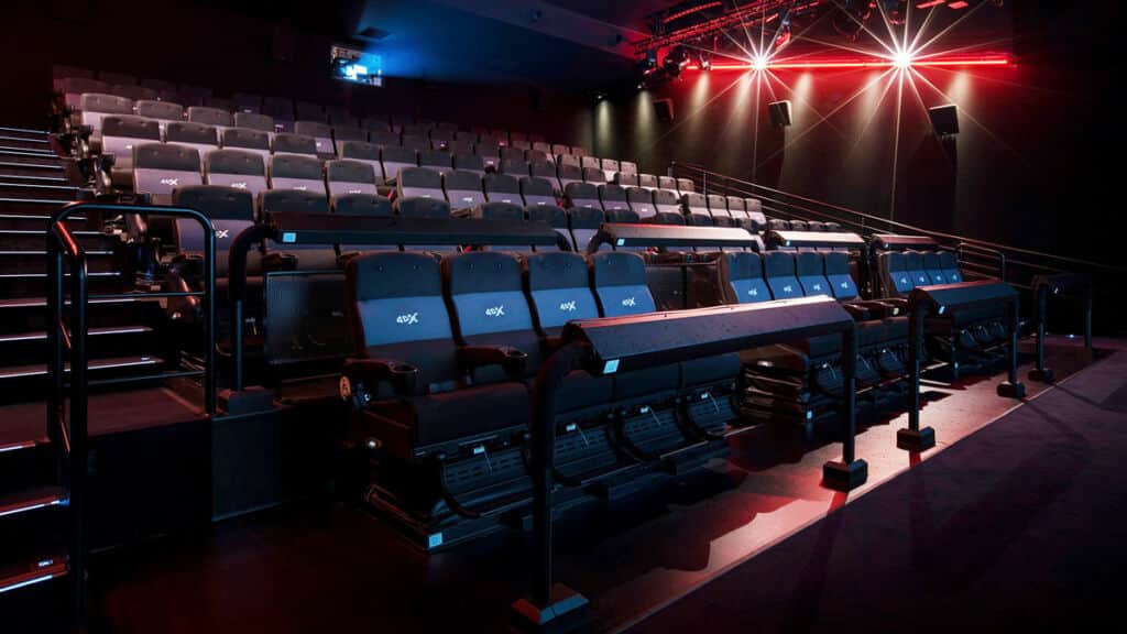Salle de cinéma vide avec des rangées de fauteuils inclinables éclairées par des lumières rouges et bleues.