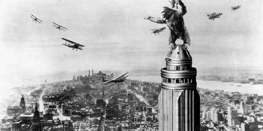 Un gorille géant au sommet d’un immeuble, entouré d’avions biplans au-dessus d’une ville.
