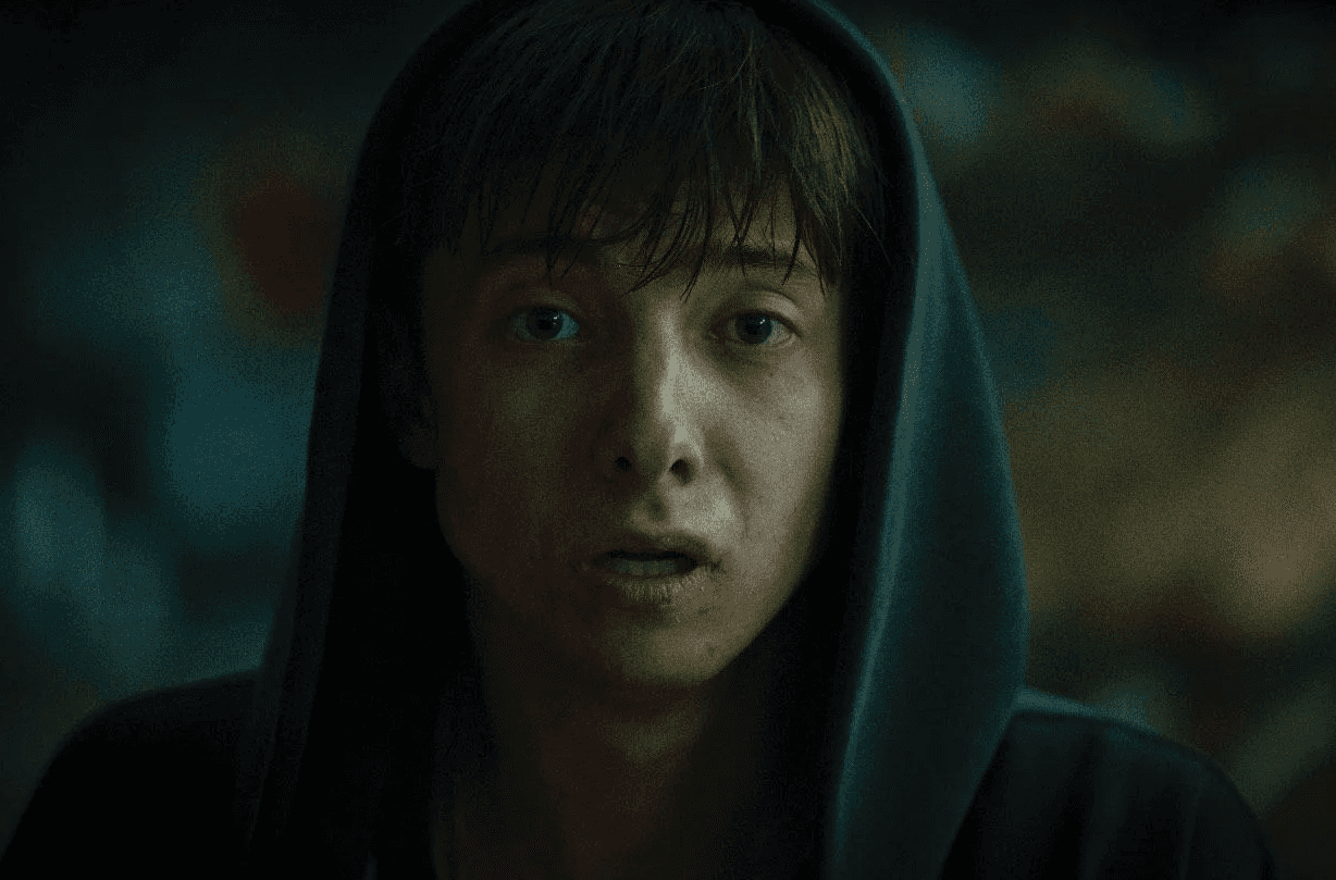 Personne encapuchonnée, le visage éclairé dans une ambiance sombre et verdâtre.