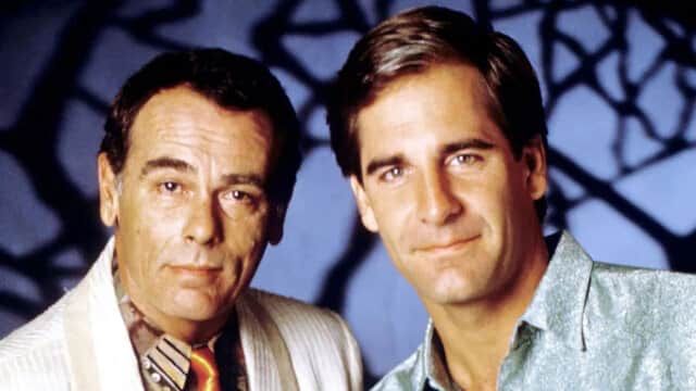 Deux hommes posant devant un fond bleu avec des ombres géométriques.