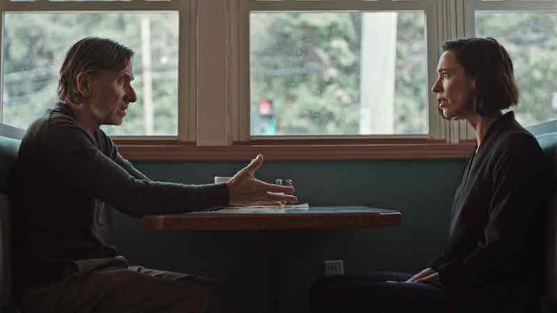 Deux personnes assises face à face dans un café, l’homme gesticulant tandis que la femme l’écoute.