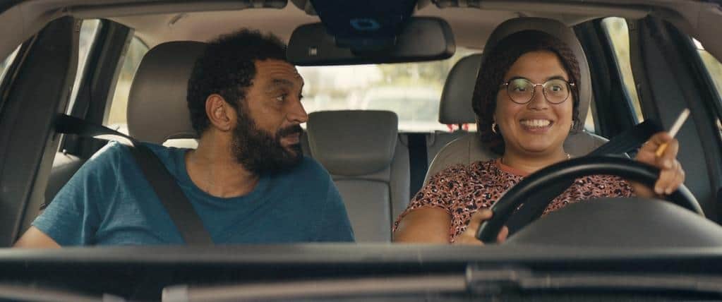Un homme barbu et une femme souriante assis à l’avant d’une voiture, la femme conduisant