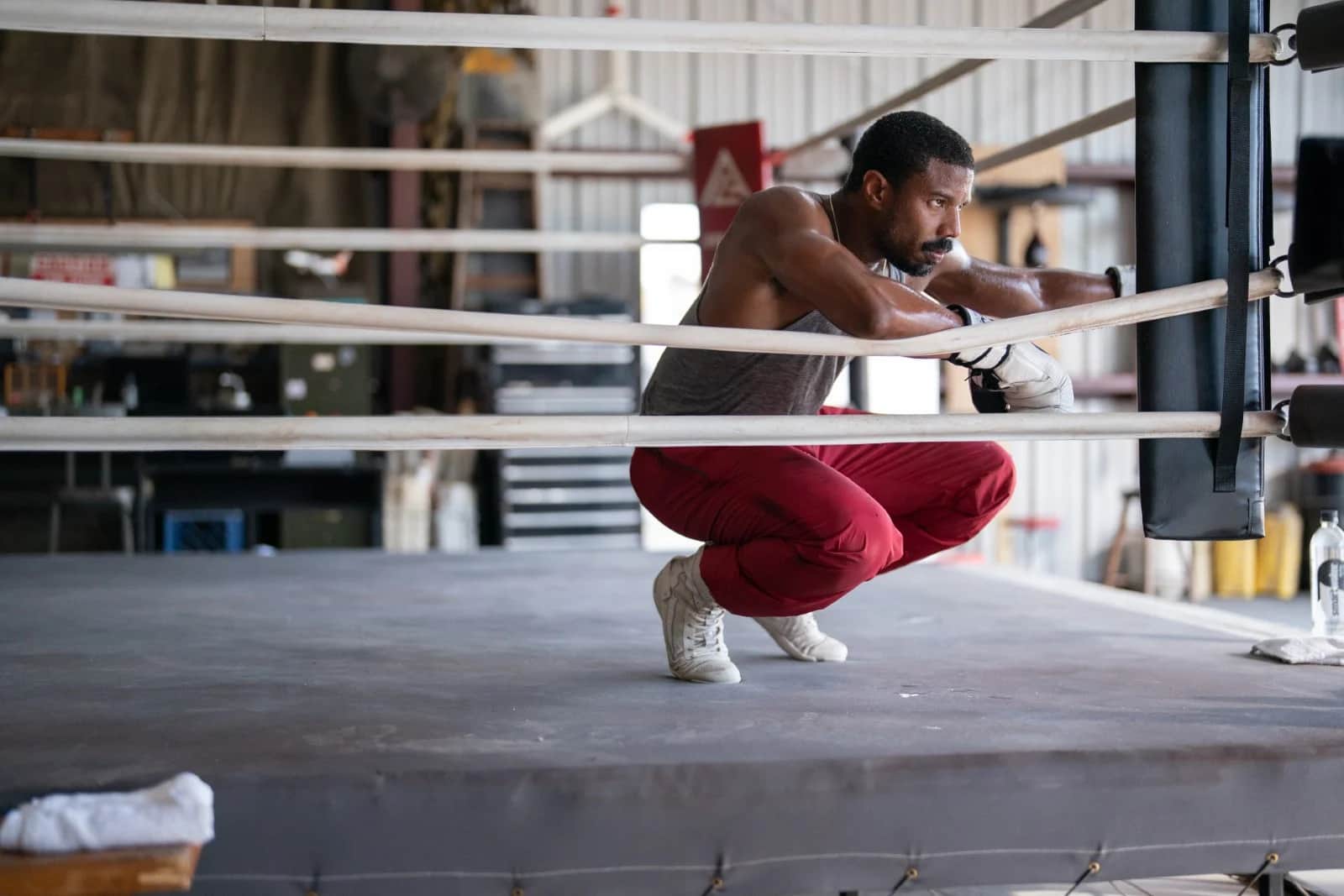 Un boxeur accroupi dans un ring, appuyé contre les cordes, portant un pantalon rouge et des gants blancs