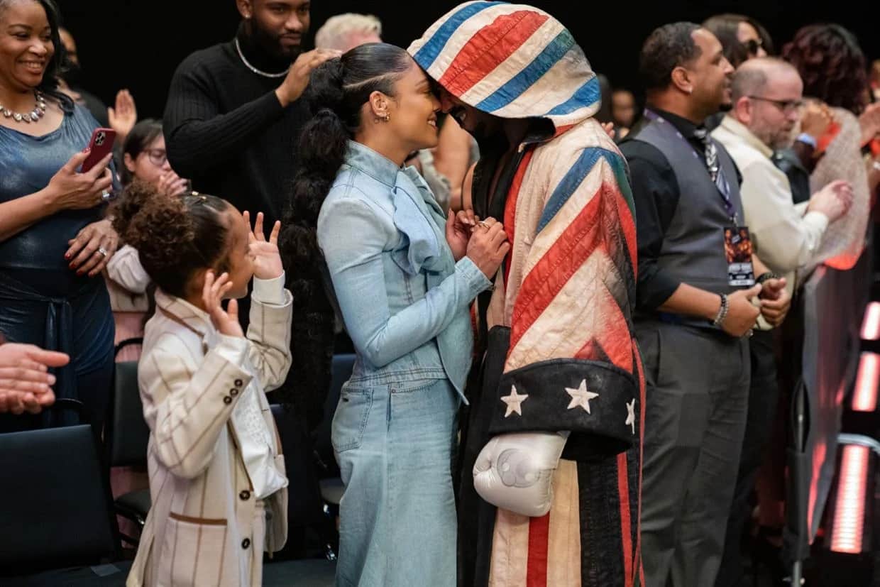 Une femme embrasse une personne vêtue d’un costume rayé rouge, blanc et bleu, entourées d’un groupe de personnes.