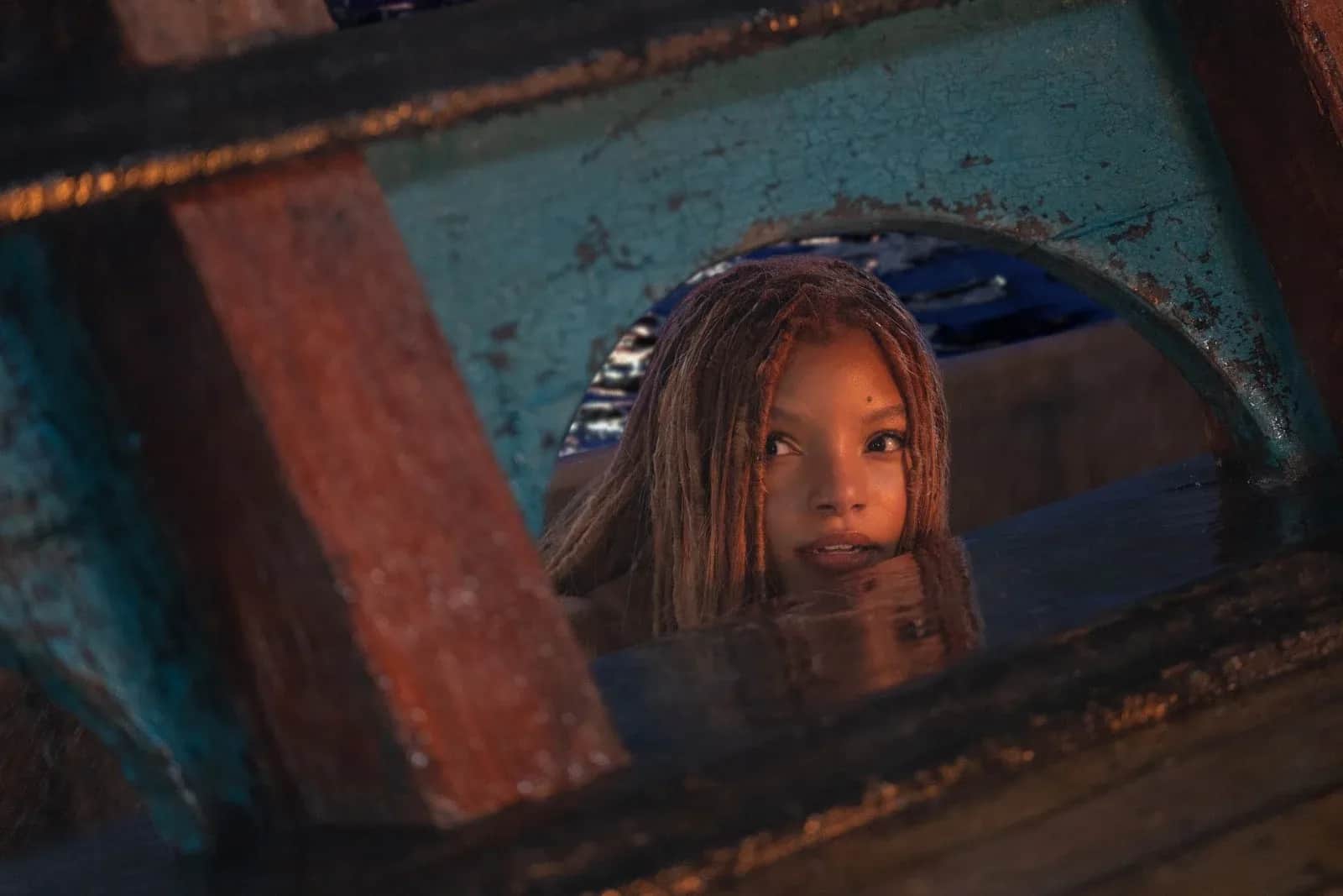 Jeune fille aux cheveux longs regardant à travers une ouverture dans une structure métallique rouillée.