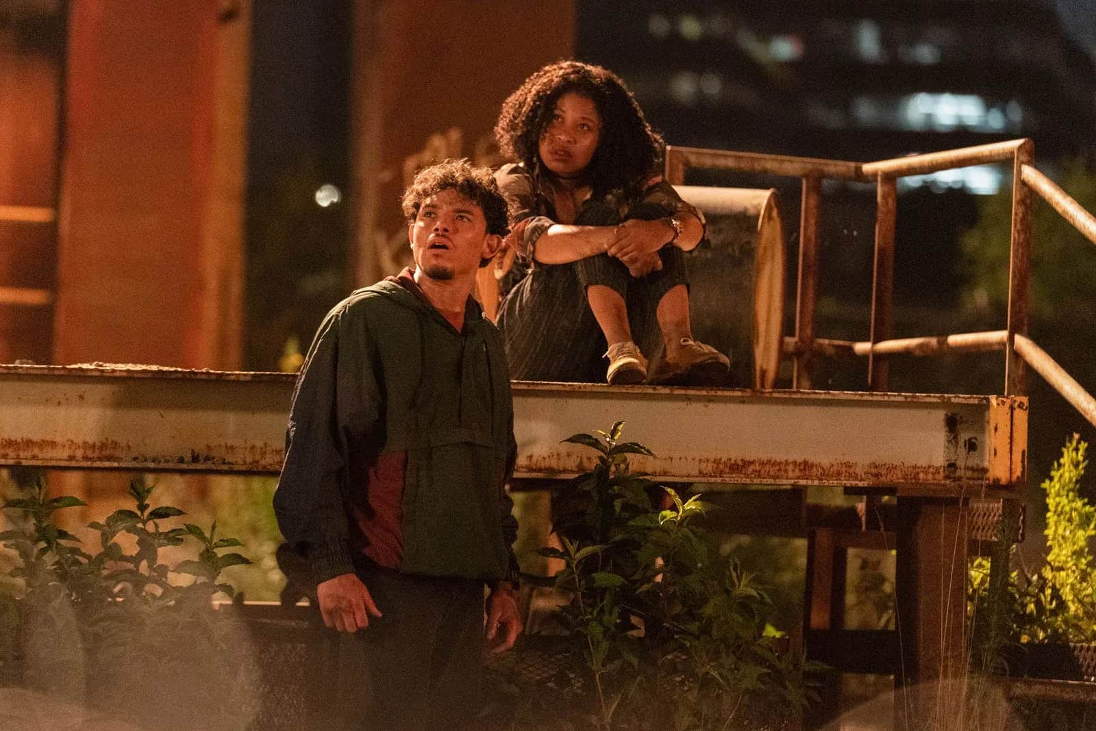 Deux personnes, un homme debout et une femme assise sur une passerelle, la nuit.