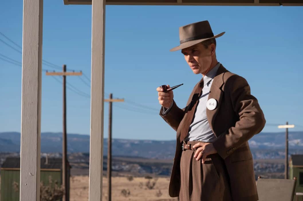 Un homme en costume et chapeau tient une pipe devant un paysage désertique, avec un badge « K-6 ».