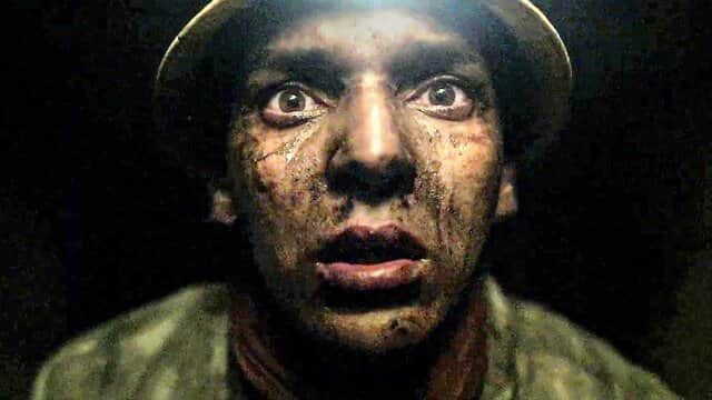Un homme au visage sale et effrayé portant un casque, éclairé par une lumière frontale dans l'obscurité.