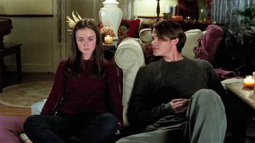Deux jeunes adultes assis sur un canapé, la jeune femme regardant devant elle et l’homme tourné vers elle dans un salon.