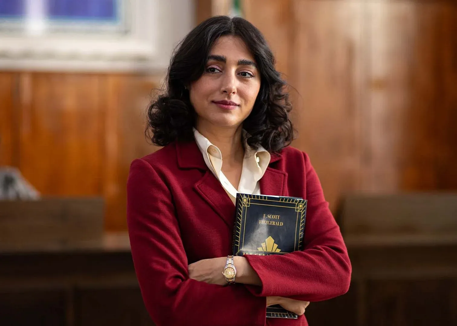 Une femme aux cheveux noirs tient un livre portant le nom « F. SCOTT FITZGERALD », dans une salle en bois.