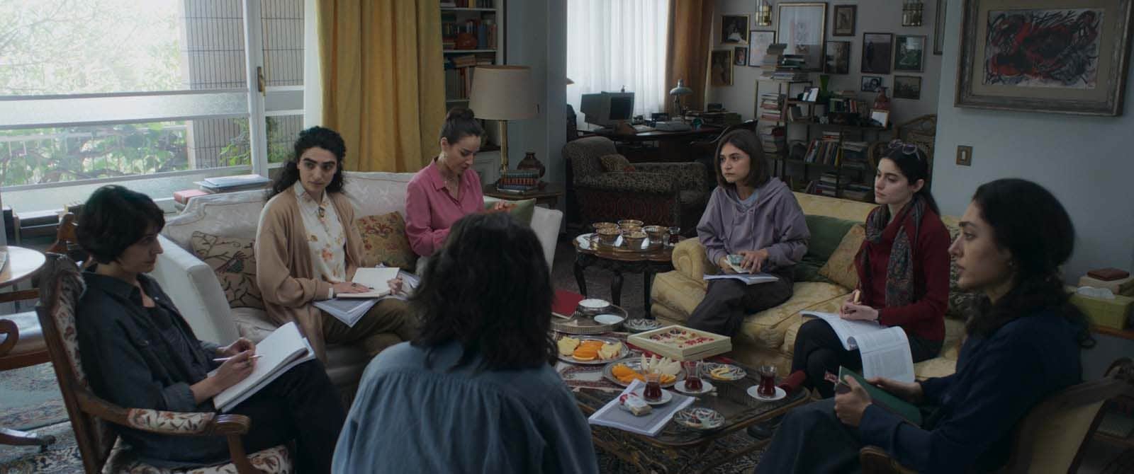 Un groupe de femmes réunies dans un salon, certaines prenant des notes autour d’une table basse.