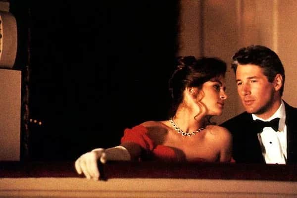 Un couple, une femme en robe rouge et un homme en smoking, accoudés à une balustrade.