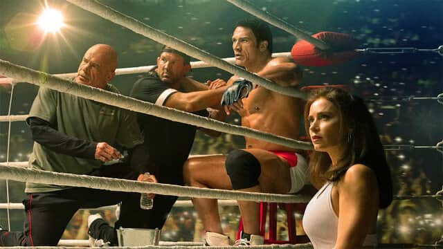 Un boxeur assis dans un coin du ring entouré de son équipe, avec une femme en avant-plan, dans une ambiance de match.