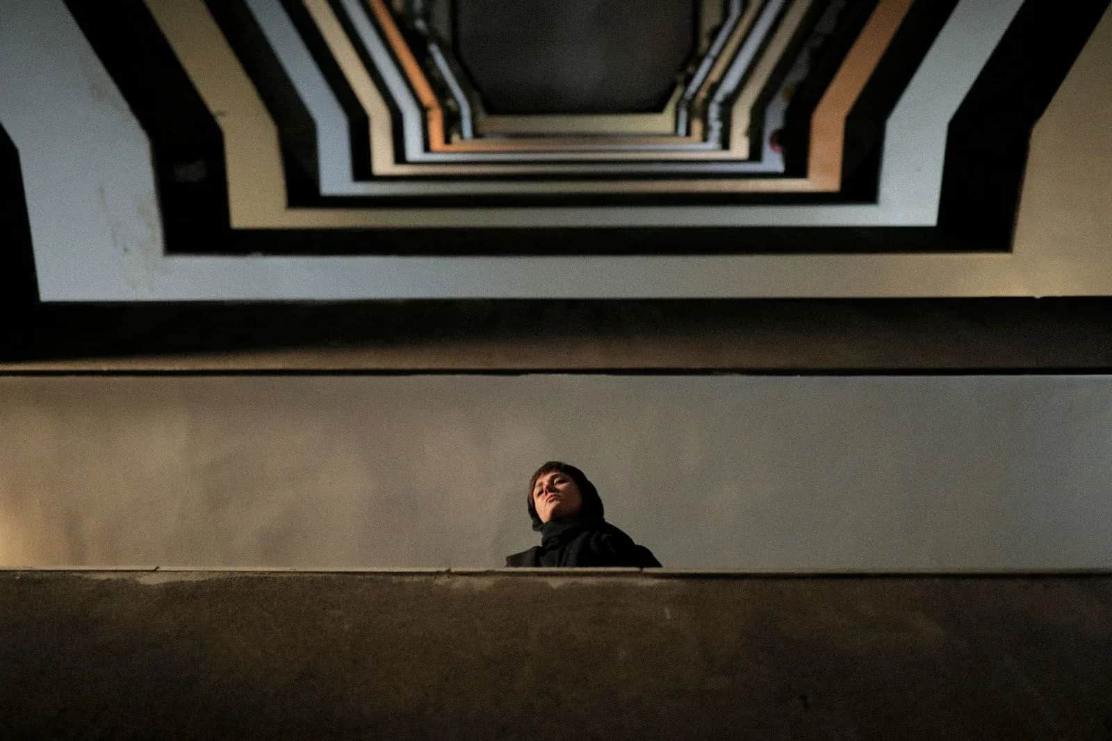 Personne vêtue de noir regardant vers le haut dans un escalier aux lignes géométriques.