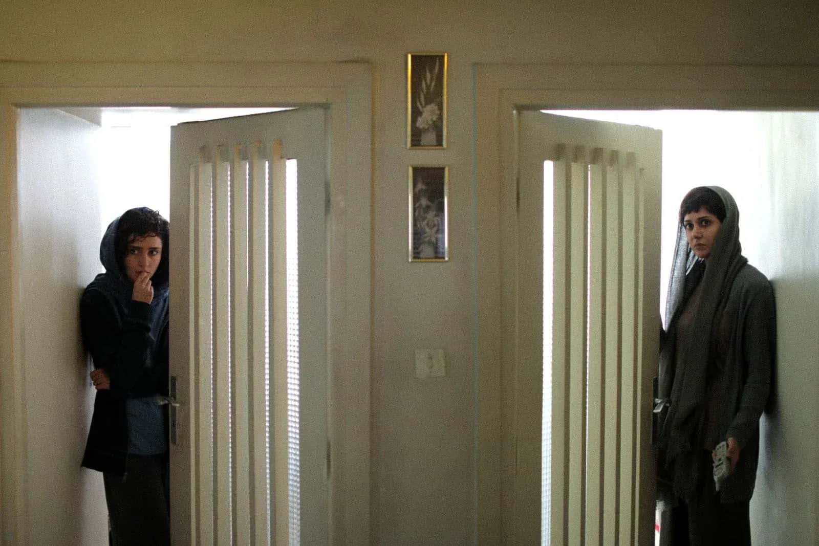 Deux femmes voilées se tiennent dans l’embrasure de deux portes ouvertes, de part et d’autre d’un couloir.