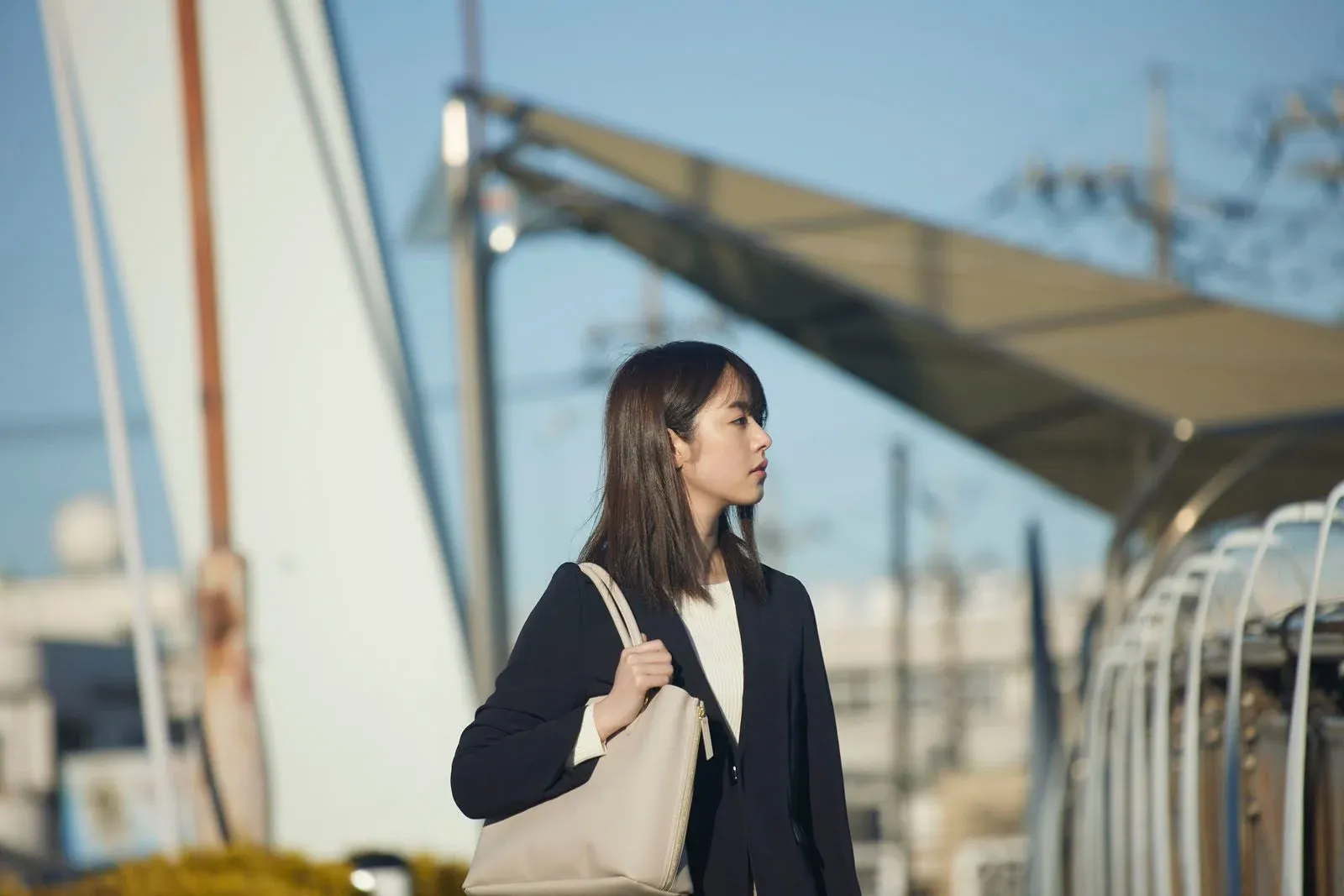 Jeune femme portant un sac, debout près d’une gare ou d’un quai sous un auvent métallique