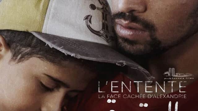 Affiche de « L’ENTENTE » montrant un homme barbu serrant un enfant endormi, avec « LA FACE CACHÉE D’ALEXANDRIE