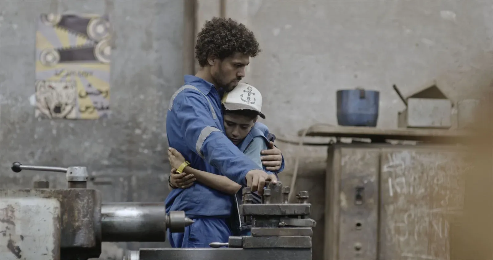 Deux ouvriers en bleu de travail se tiennent près d’un tour métallique dans un atelier.