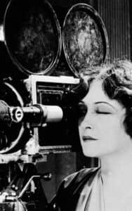 Femme observant une caméra de cinéma ancienne en noir et blanc
