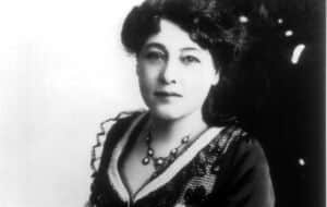 Portrait en noir et blanc d’une femme aux cheveux foncés, portant un collier et une robe ornée de dentelle.