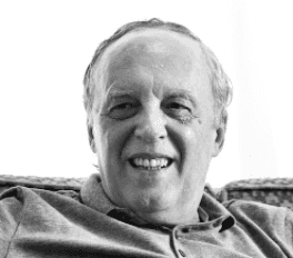Portrait en noir et blanc d’un homme âgé souriant, assis sur un canapé.