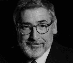 Portrait en noir et blanc d’un homme portant des lunettes rondes, une barbe et une cravate.