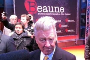 Un homme aux cheveux blancs en costume devant un groupe de personnes, au festival « Beaune » du film policier.