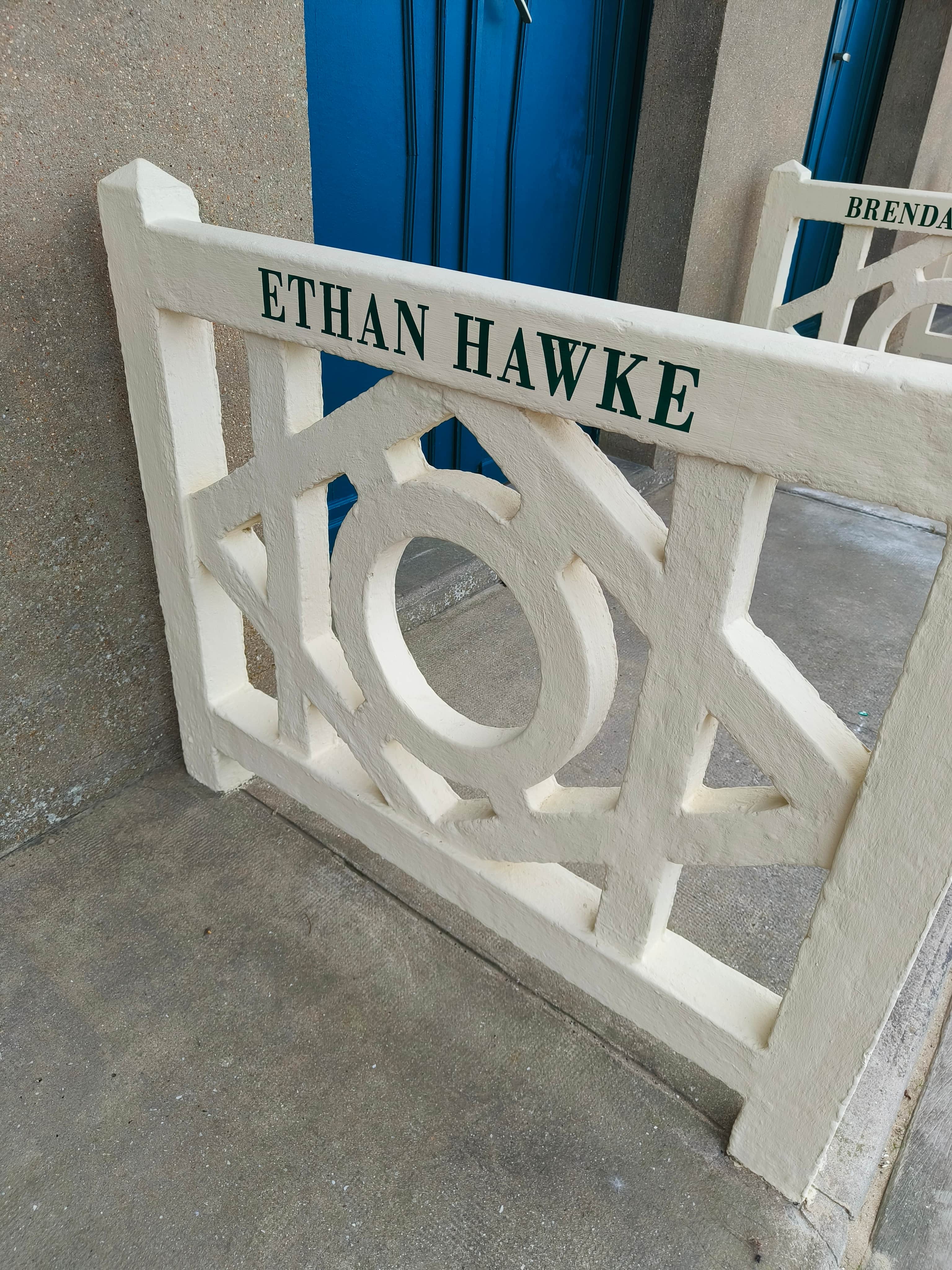Chaise de cinéma blanche portant l’inscription « ETHAN HAWKE », devant une porte bleue.