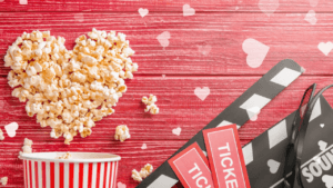 Cœur en pop-corn avec un seau rayé, un clap de cinéma et des tickets sur fond rouge.