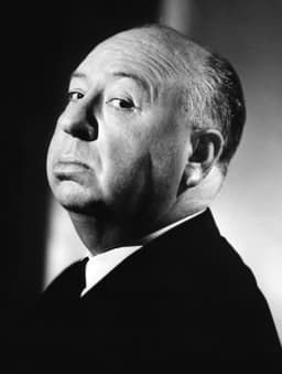 Alfred Hitchcock en gros plan, en costume sombre, regardant la caméra en noir et blanc