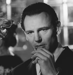 Homme fumant une cigarette, en gros plan dans un intérieur en noir et blanc.