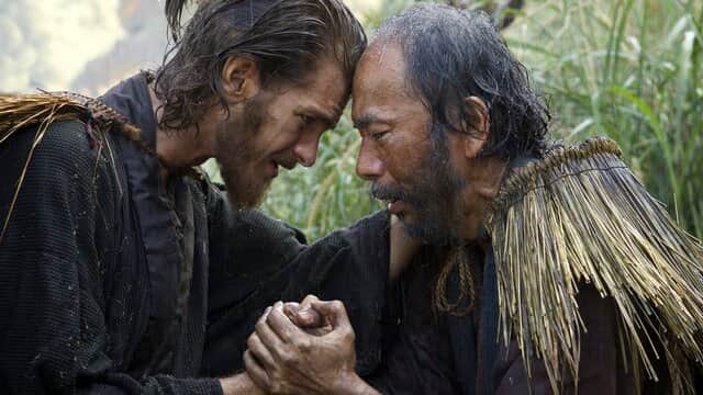 Deux hommes se tenant la main, tête contre tête, dans un champ d'herbes hautes.