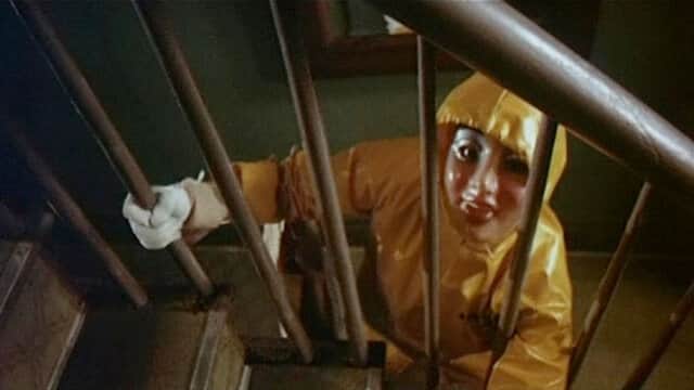 Personne en combinaison jaune montant un escalier, vue à travers la rampe.