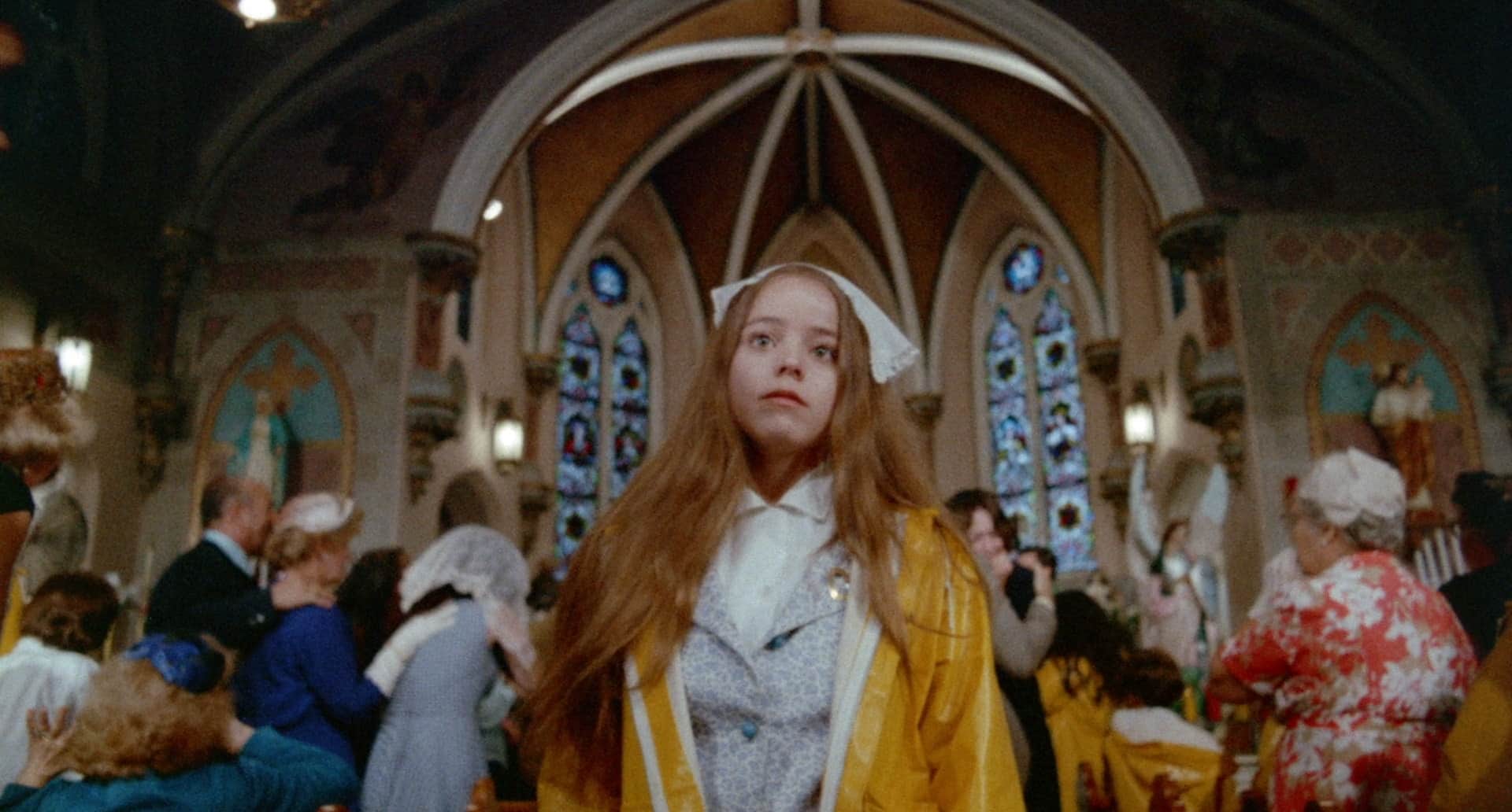 Jeune femme rousse en imperméable jaune au centre d’une cérémonie dans une église ornée de vitraux