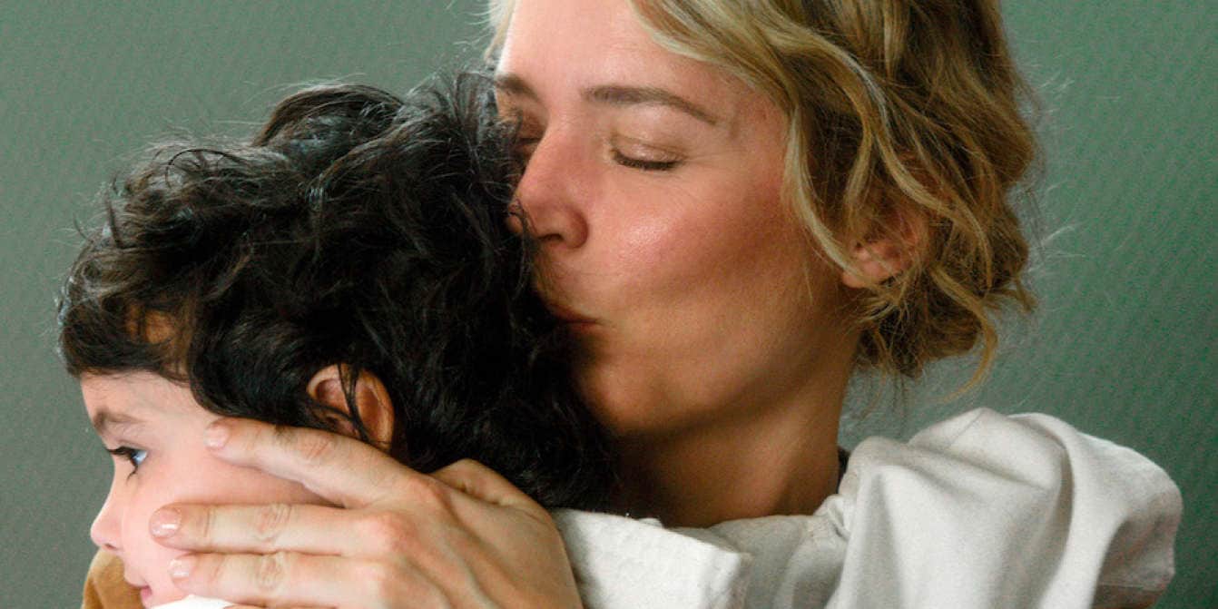Une femme embrasse la tête d’un enfant aux cheveux bouclés, qu’elle enlace contre elle.