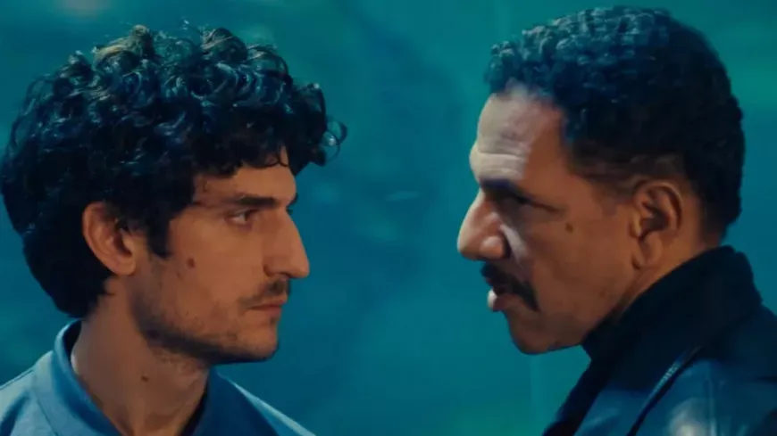 Deux hommes se font face, très près l’un de l’autre, sur un fond bleu indistinct.