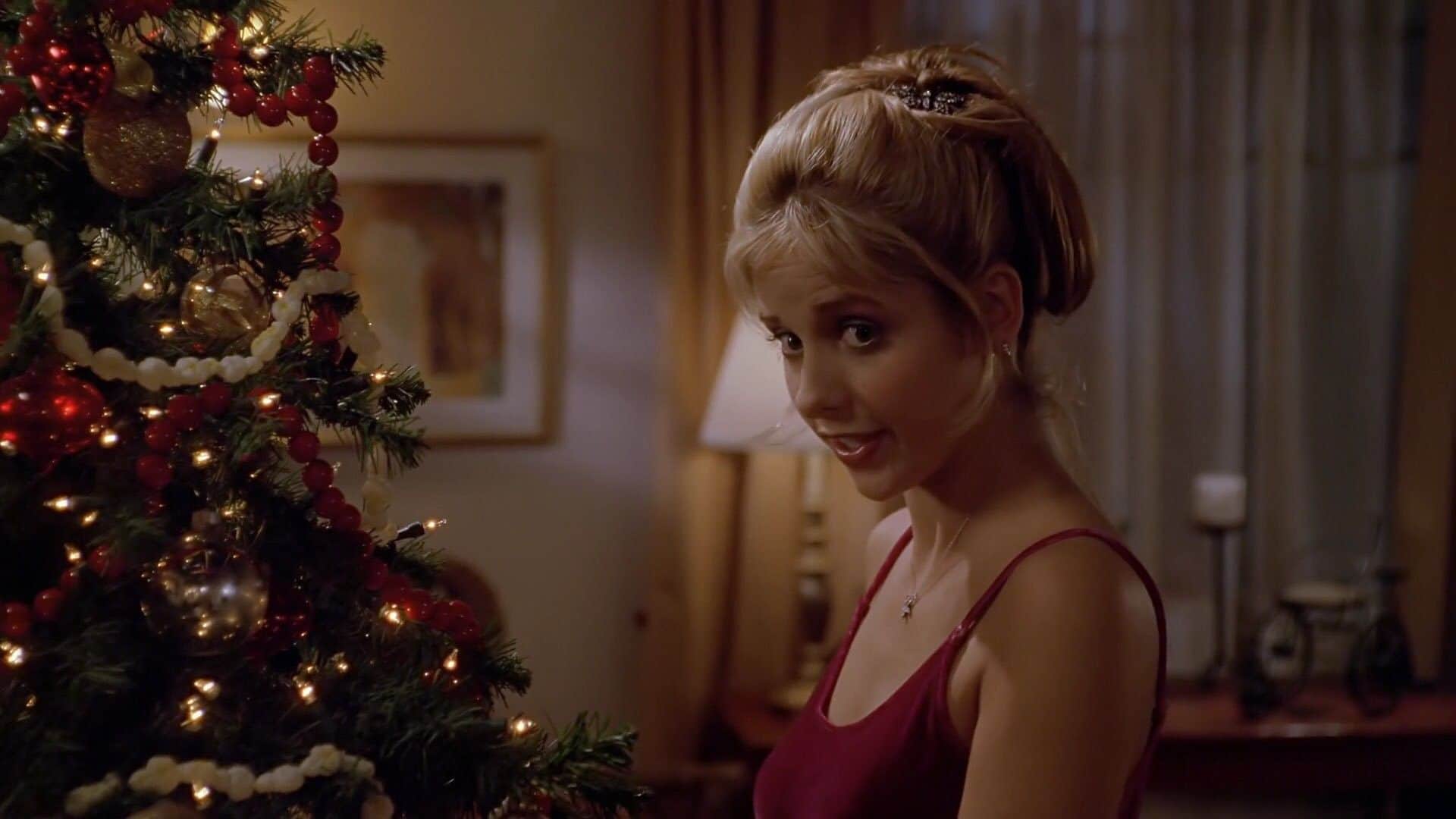 Une femme près d’un sapin de Noël décoré, dans un intérieur éclairé chaleureusement.