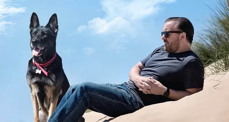 Un homme allongé sur une dune à côté d’un chien noir, sous un ciel bleu