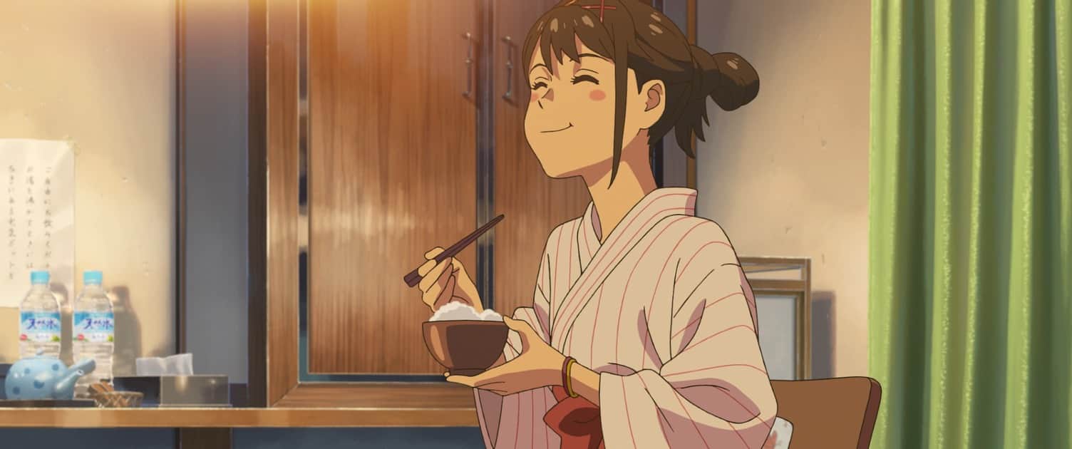Jeune femme en kimono mangeant avec des baguettes, assise dans une pièce.