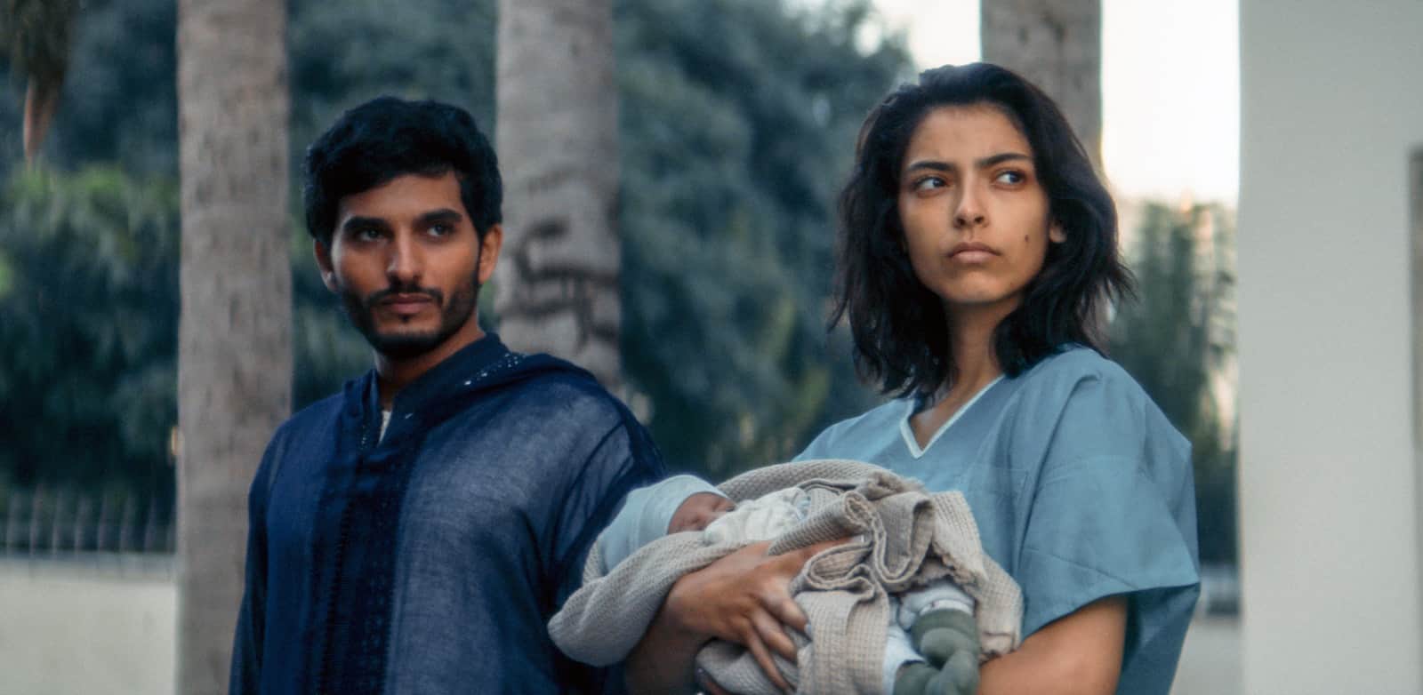 Un homme et une femme, dont une infirmière, portent un bébé emmailloté à l’extérieur.
